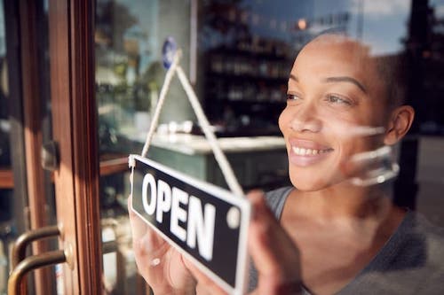 image of a female with a new business flipping a sign from closed to open!